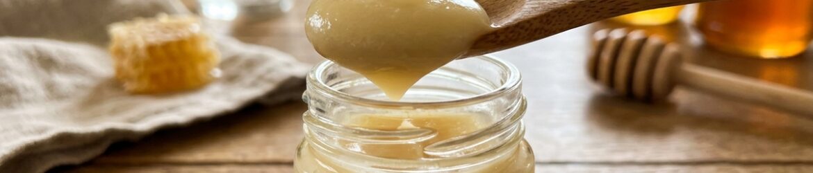 Cuillère contenant de la gelée royale jaune pâle, au-dessus d’un petit pot en verre
