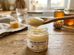 Cuillère contenant de la gelée royale jaune pâle, au-dessus d’un petit pot en verre