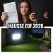 Femme inquiète tenant une facture d'électricité EDF face à la hausse des prix 2026, avec un projecteur solaire LED puissant éclairant un jardin de maison en arrière-plan.