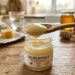 Cuillère contenant de la gelée royale jaune pâle, au-dessus d’un petit pot en verre